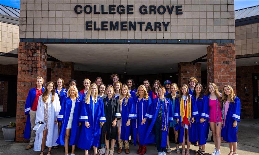 Graduating seniors smile in front of an elementary school